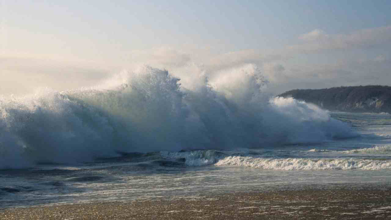 large waves crashing into the shore on a sunny day