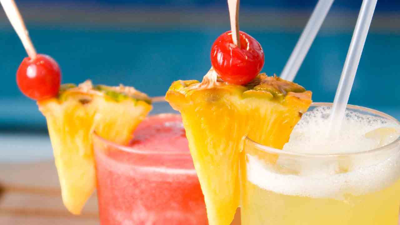 three drinks with pineapple and cherries sitting on top of a wooden table