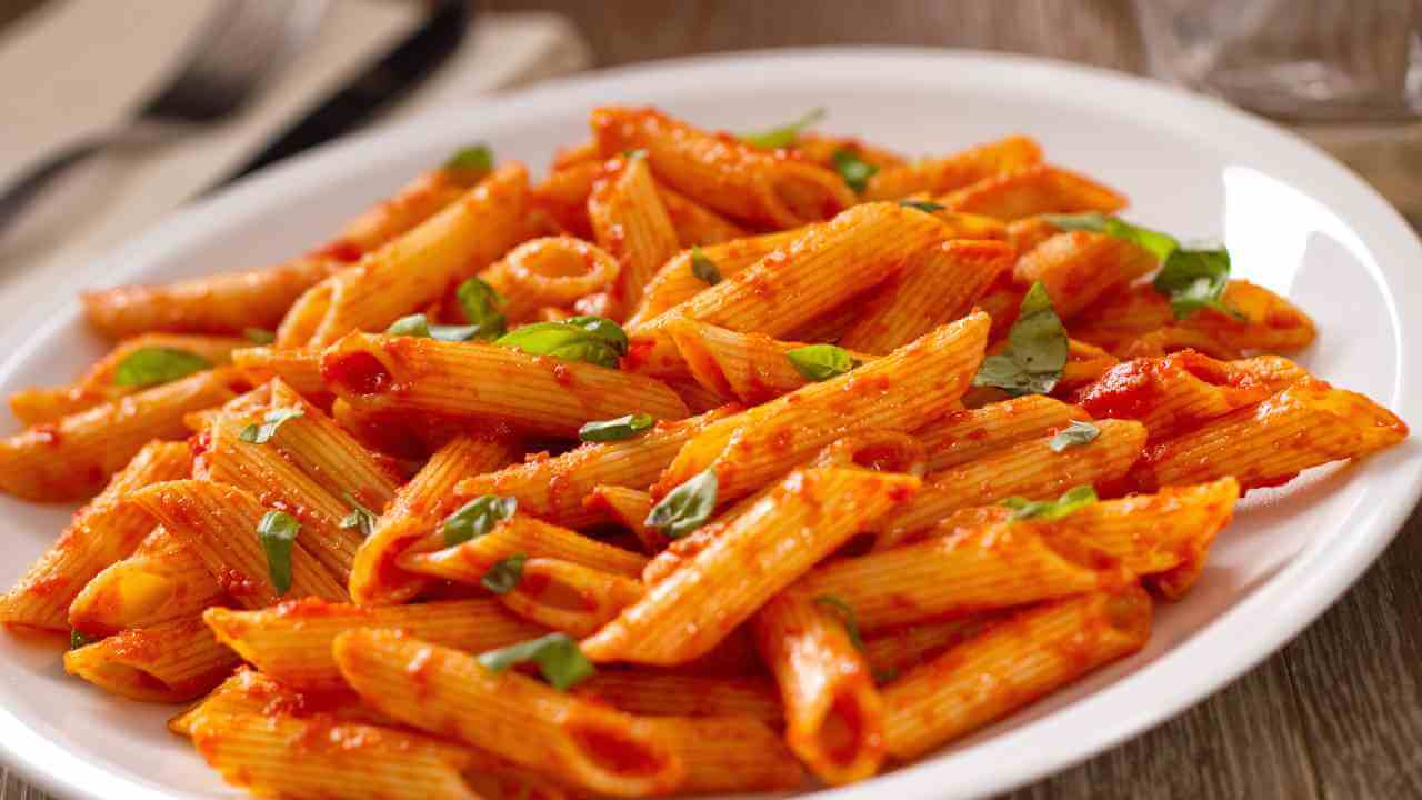 a plate of penne pasta with tomato sauce on a wooden table