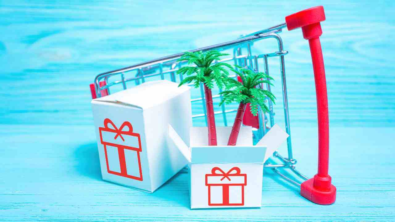 a shopping cart with a gift box and a palm tree on a blue wooden background