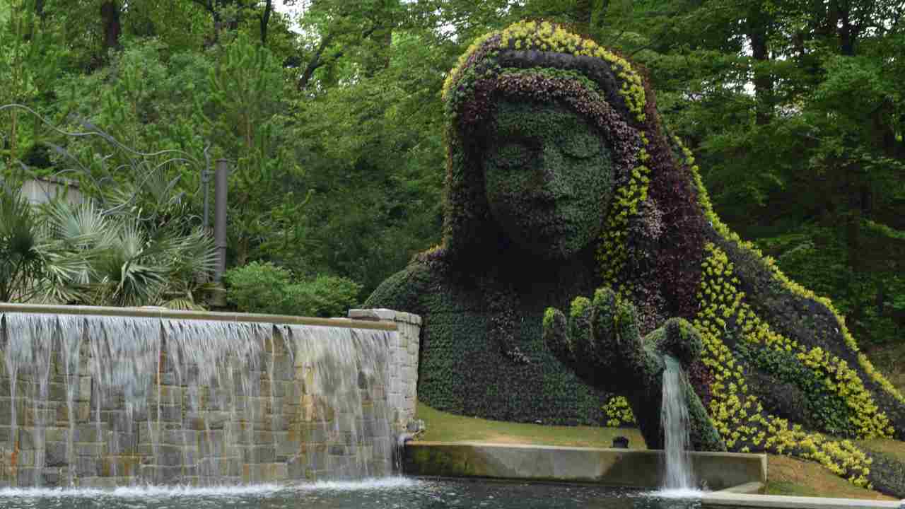 a statue made out of plants in front of a fountain