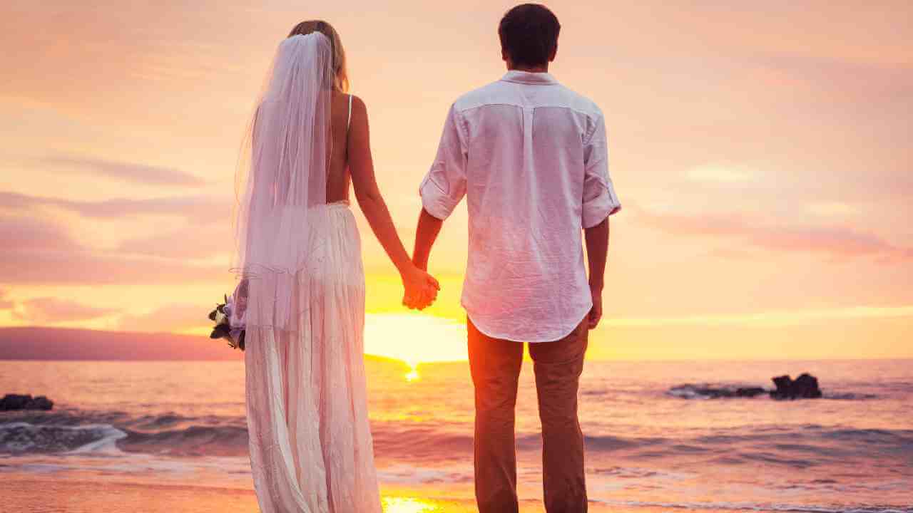 A bride and groom holding hands on the beach at sunset