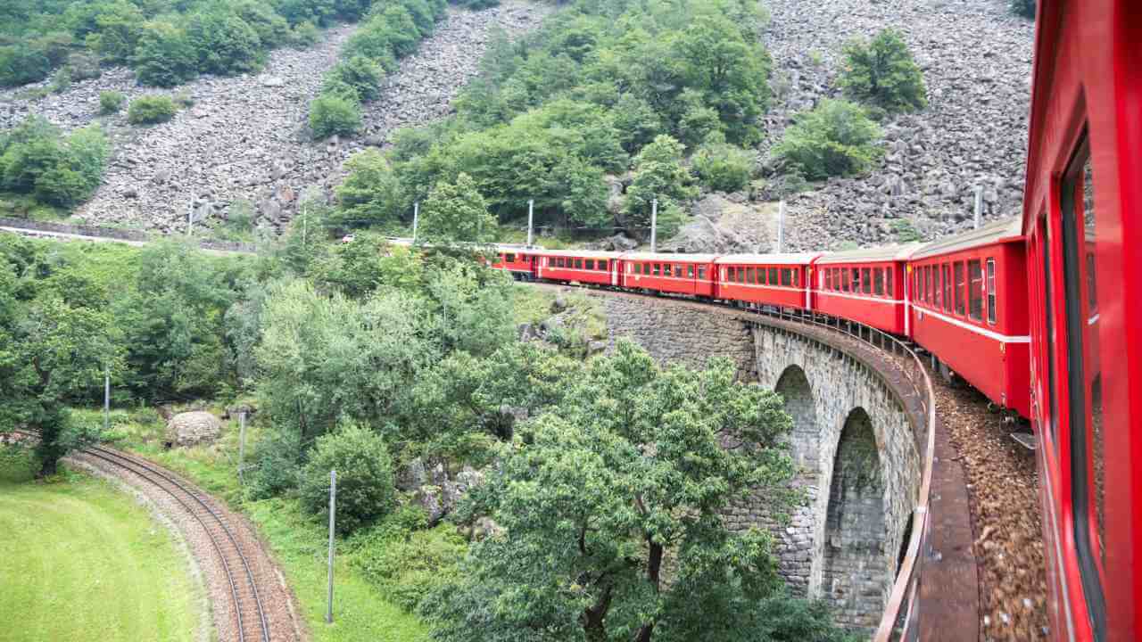 a red train traveling over a bridge in the mountains
