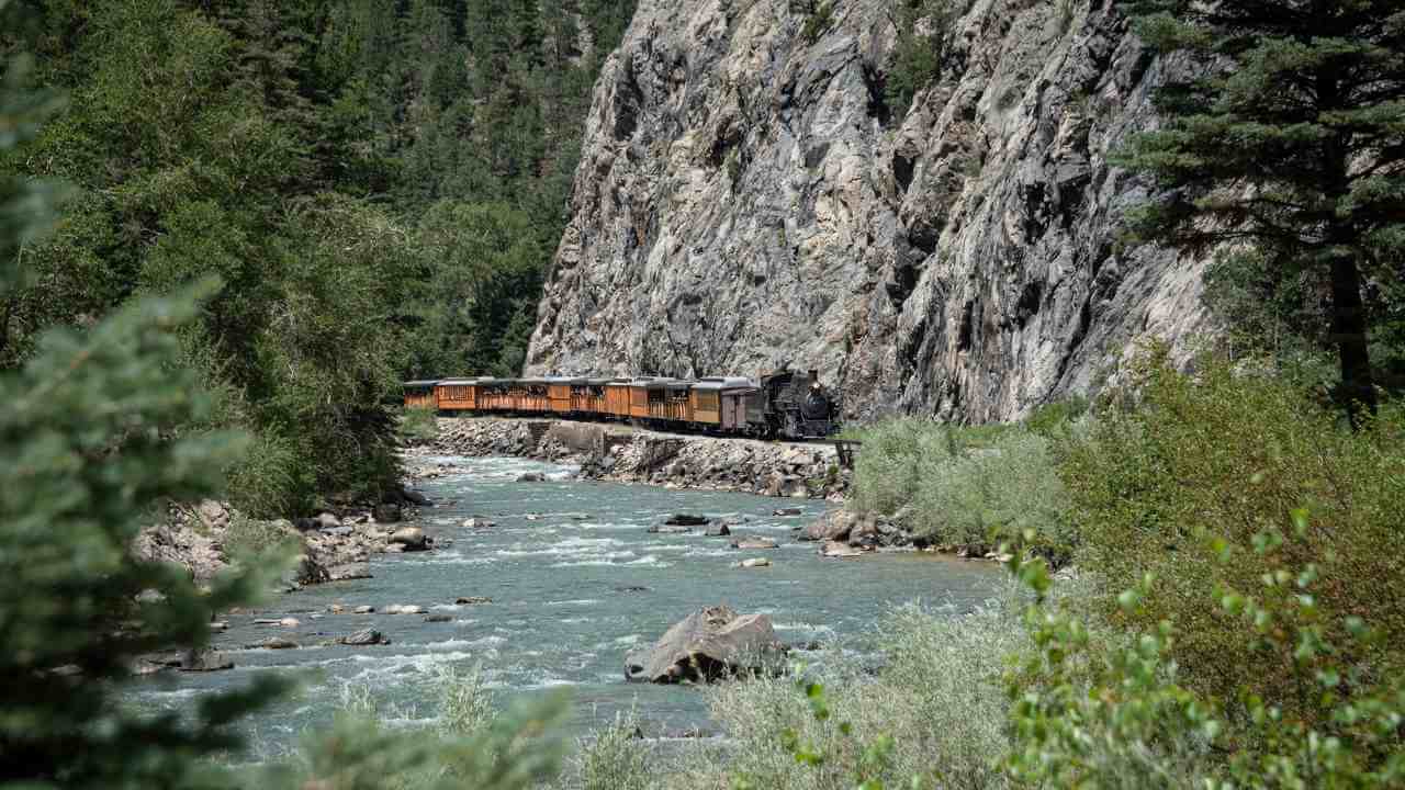a train traveling through the mountains near a river