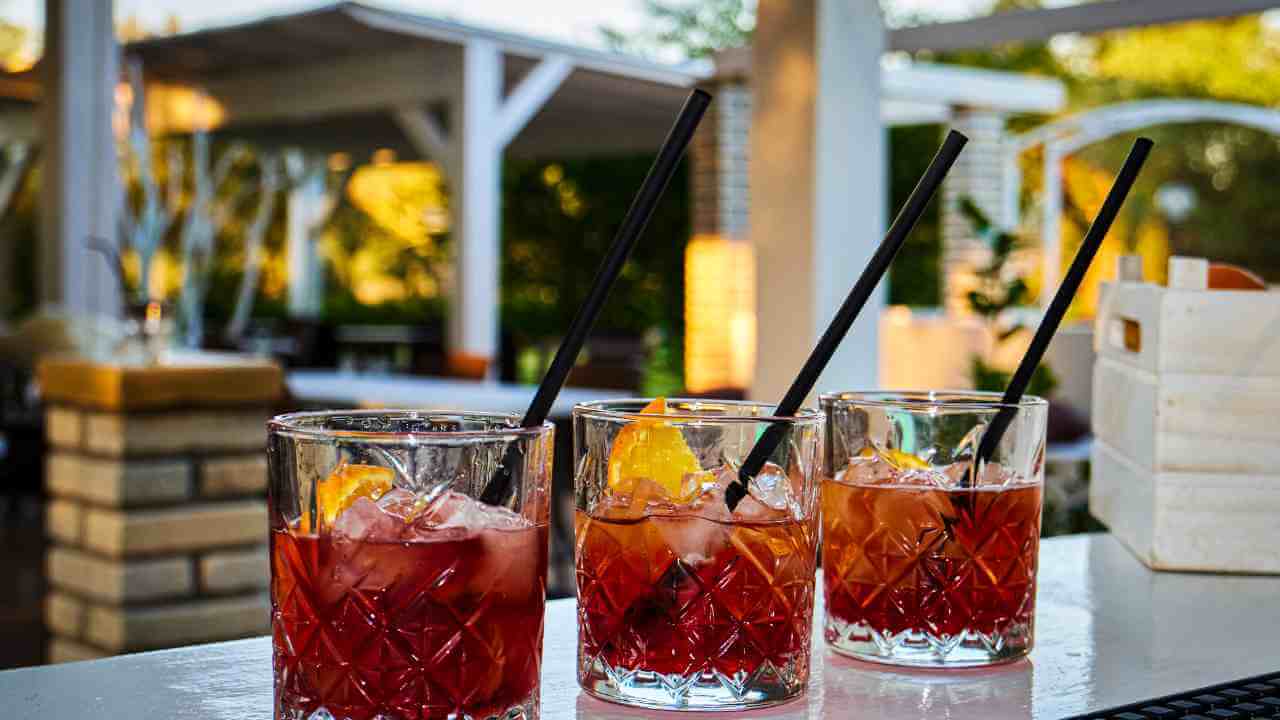 three glasses of red drink with straws on a bar