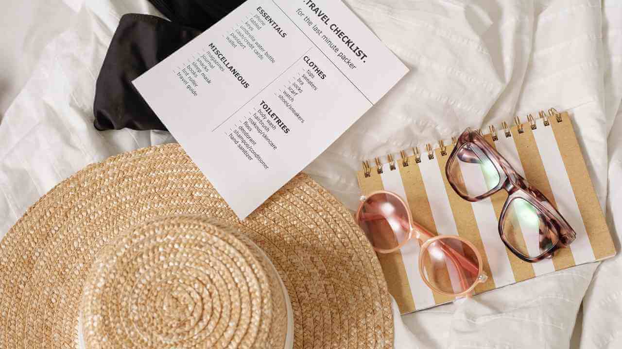 a straw hat, sunglasses and notebook on a bed