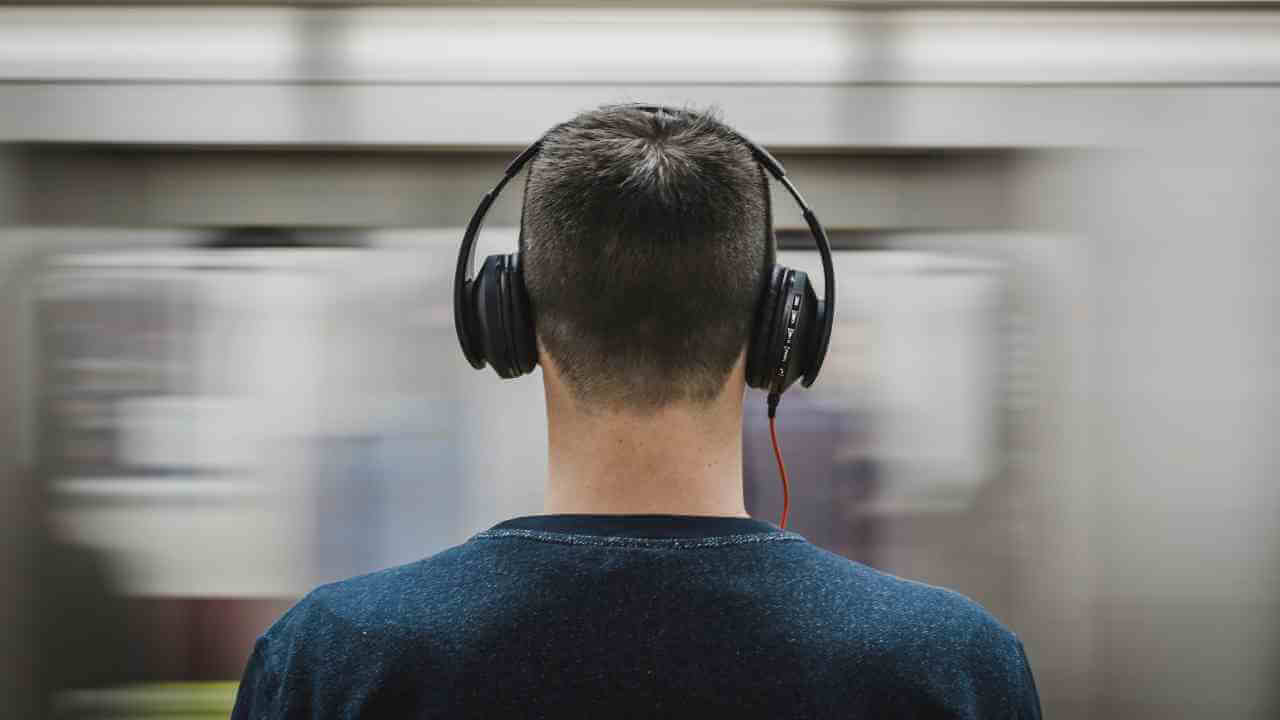 a person wearing headphones stands in front of a subway train