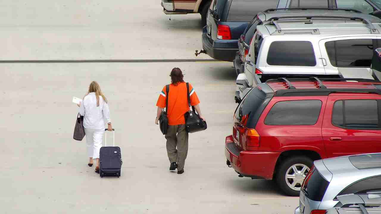 two people walking with luggage in a parking lot