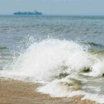 waves crashing on the beach with a ship in the background