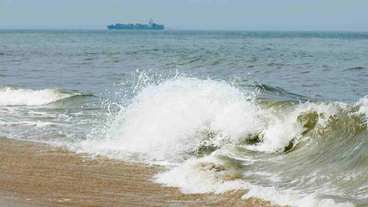 waves crashing on the beach with a ship in the background