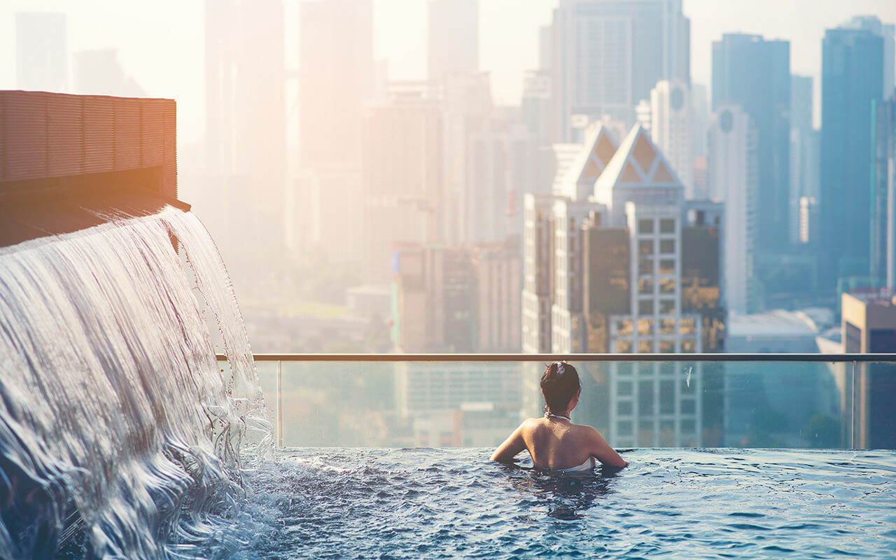 young woman enjoying the city view from roof top swimming pool.