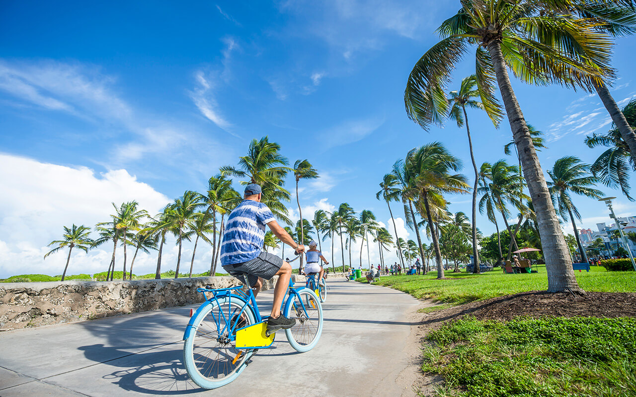 Tourists ride bicycles along the beachfront promenade in Lummus Park adjacent to historic Ocean Drive in South Beach, Miami, Florida, USA