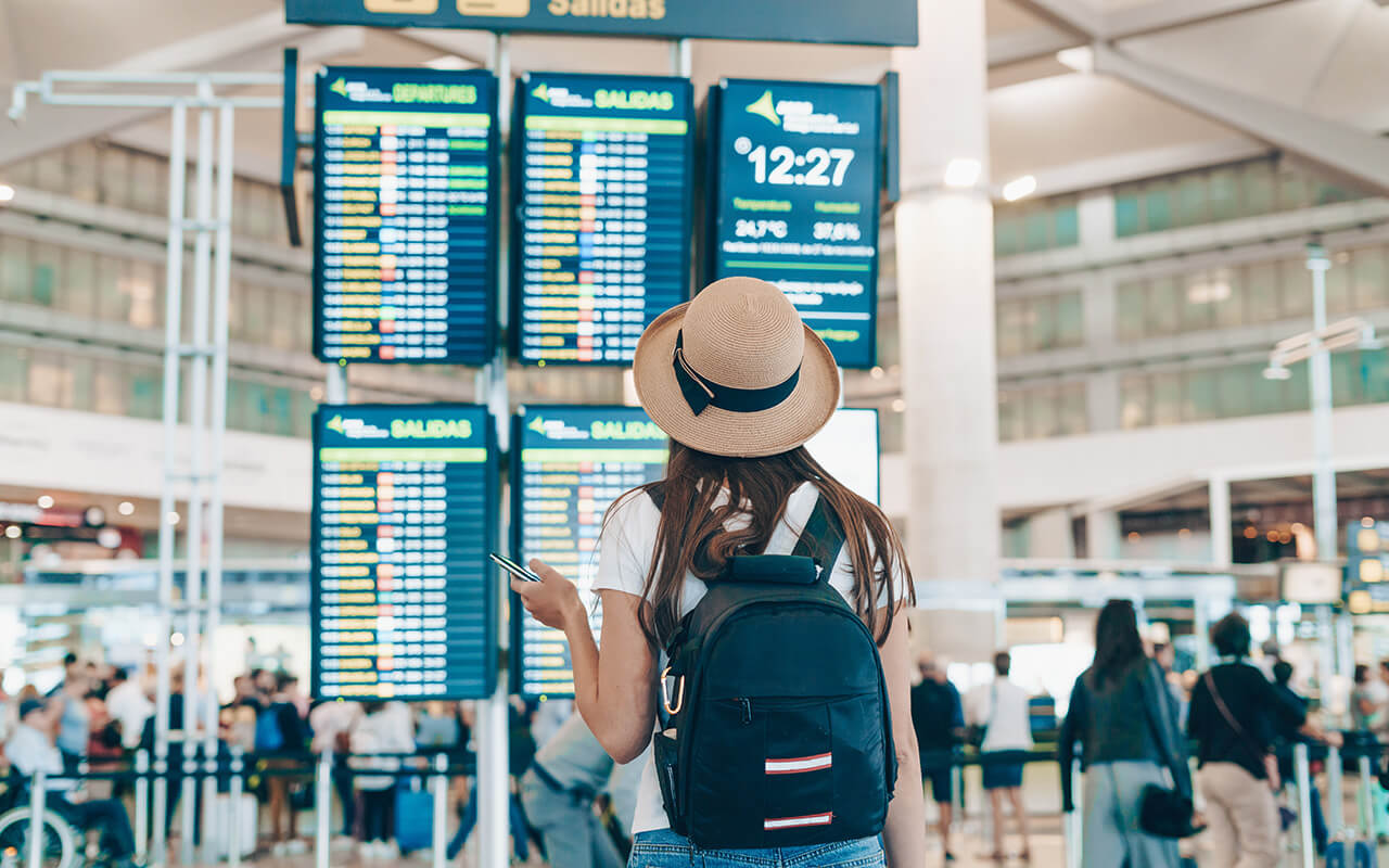 Woman in a hat looking at the departures board at an airport