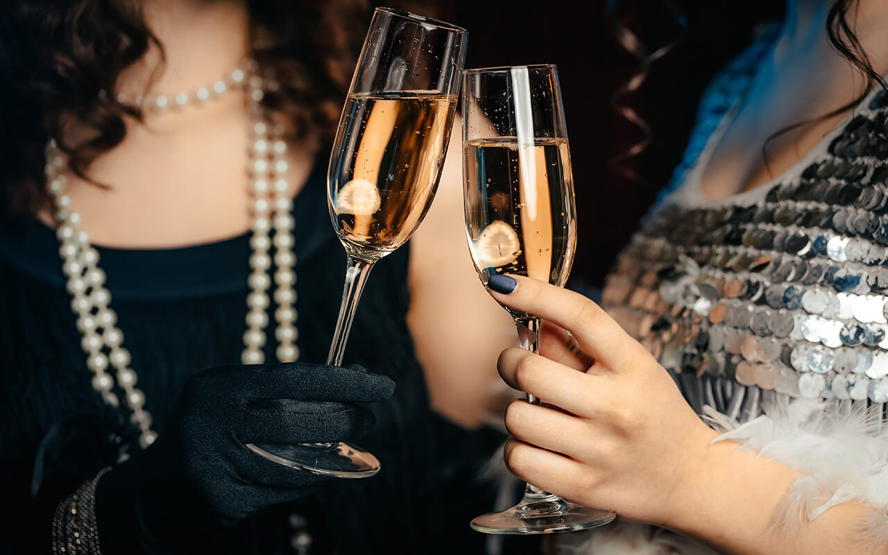 Two women dressed in vintage formalwear drink champagne 