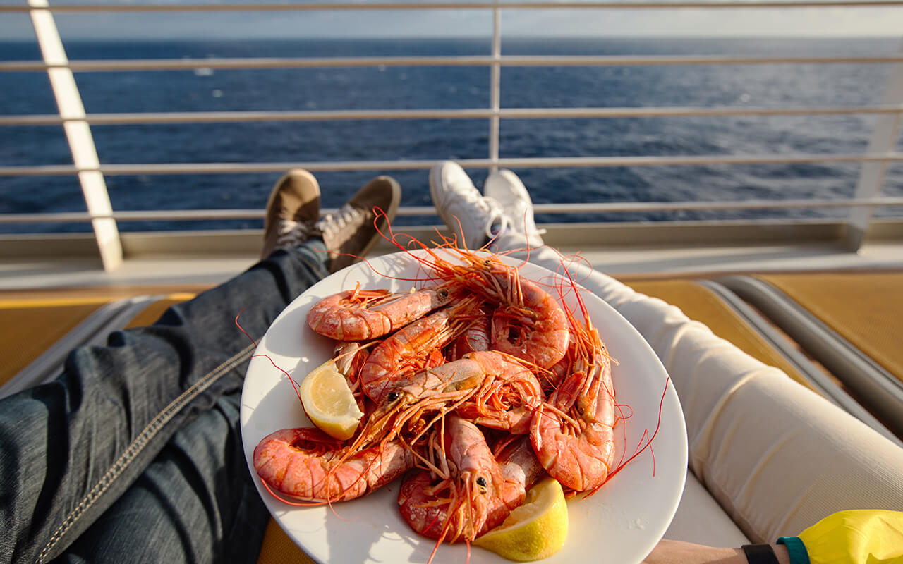 a young couple holds a plate with shrimps while on a cruise ship
