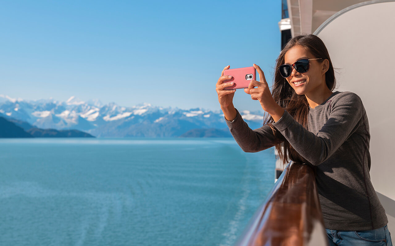 Alaska Glacier bay cruise ship travel tourist looking at icebergs taking pictures using phone in inside passage from balcony deck.