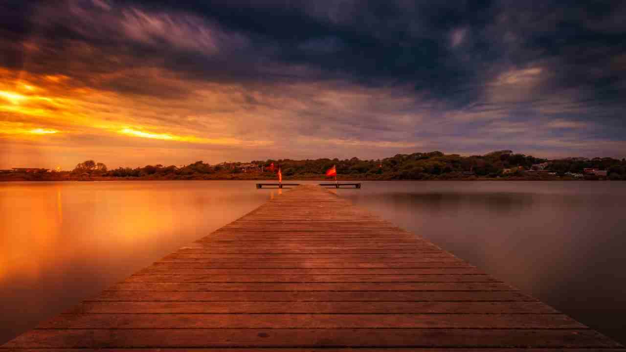 a long exposure photo of a dock in the middle of a lake at sunset