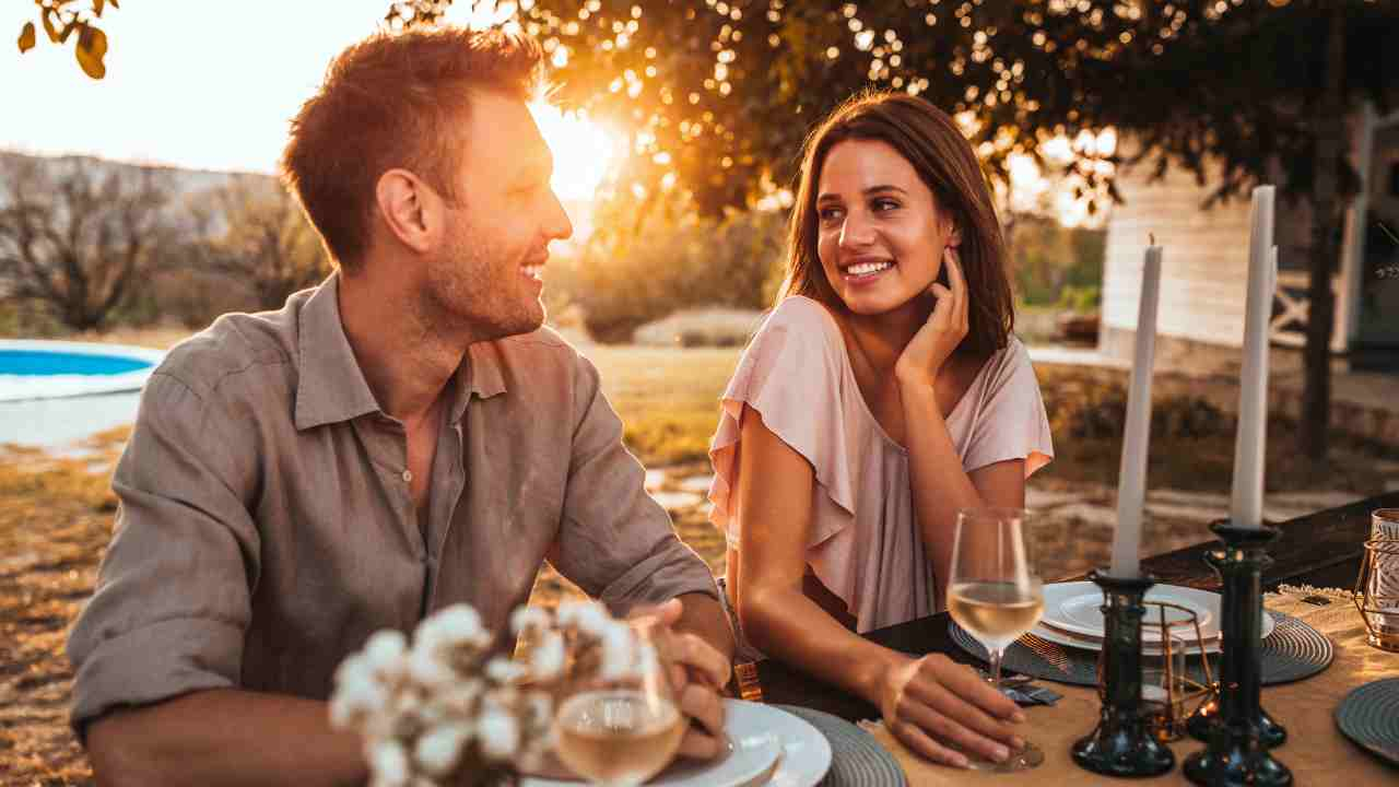 Two people sitting at a table in front of a swimming pool at sunset