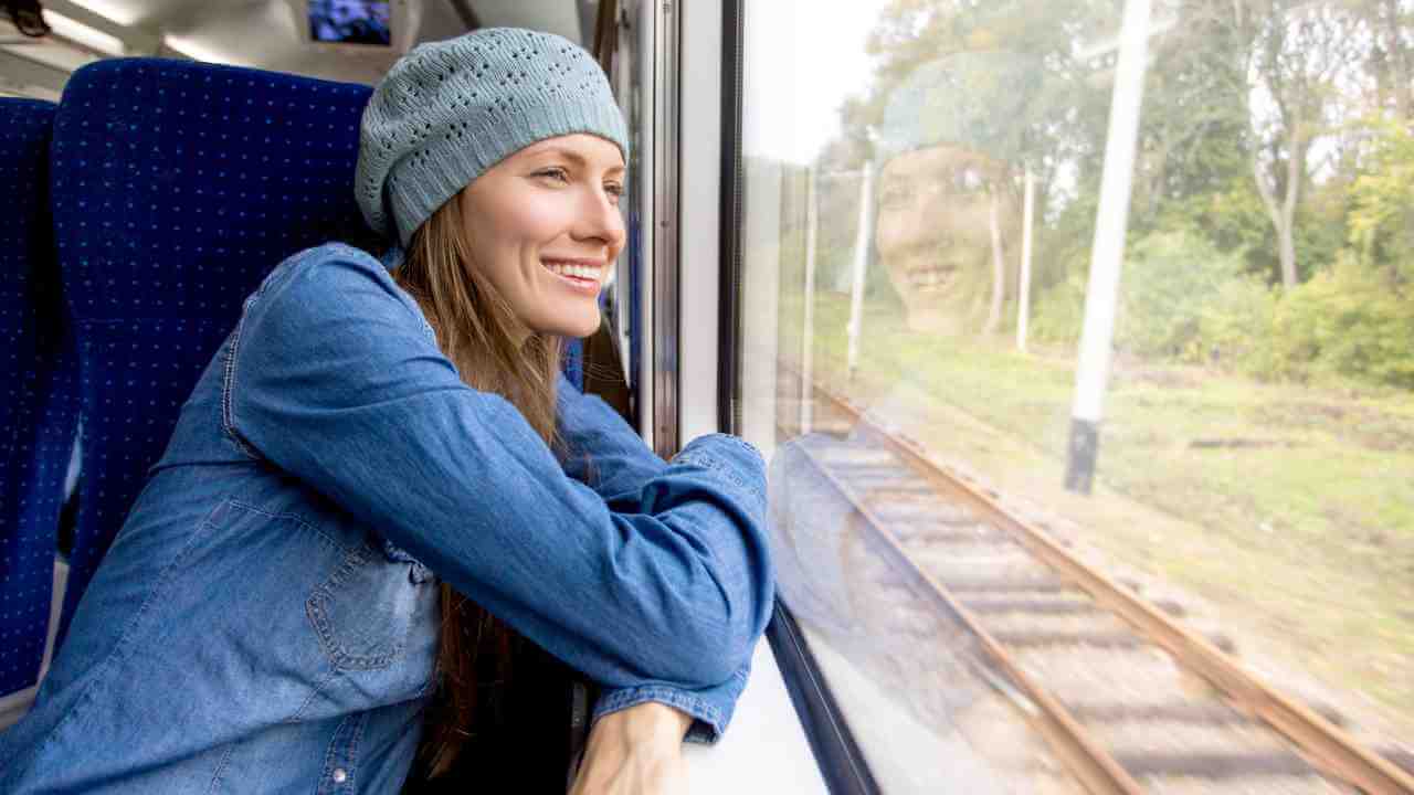 a person smiles as they look out the window of a train