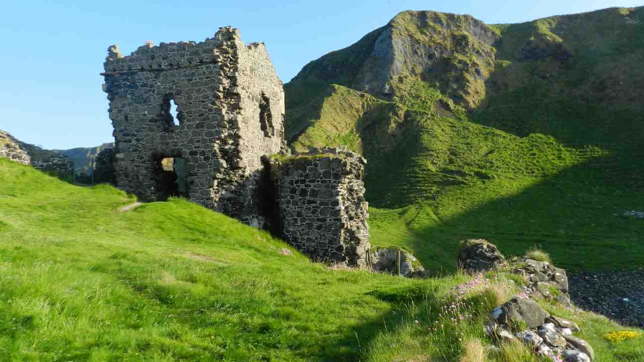 an old stone building sits on top of a grassy hill