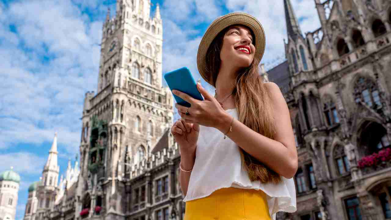 a person in a hat and yellow skirt is looking at their phone in front of a building in munich, germany