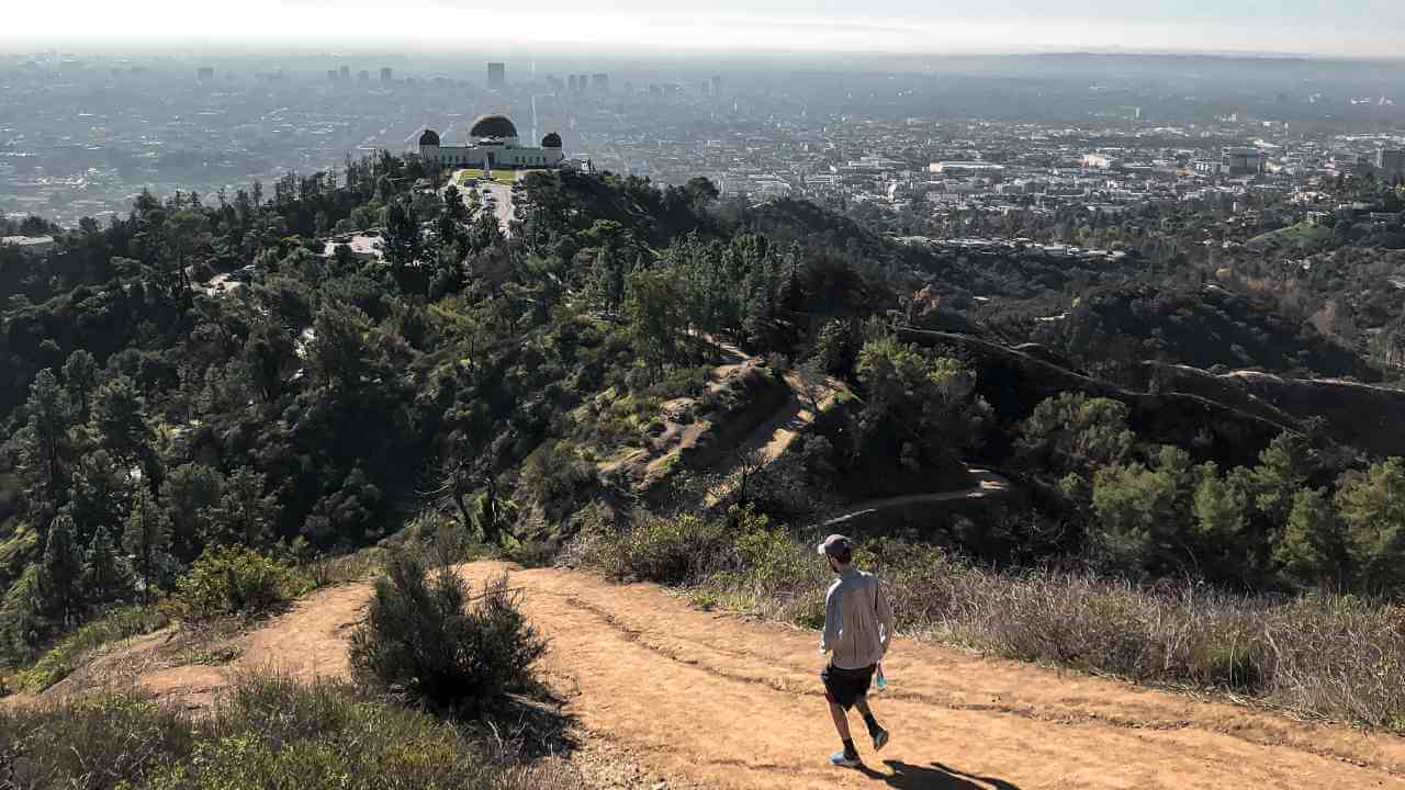 a person is running on a trail in front of the griffith observatory in los angeles, california