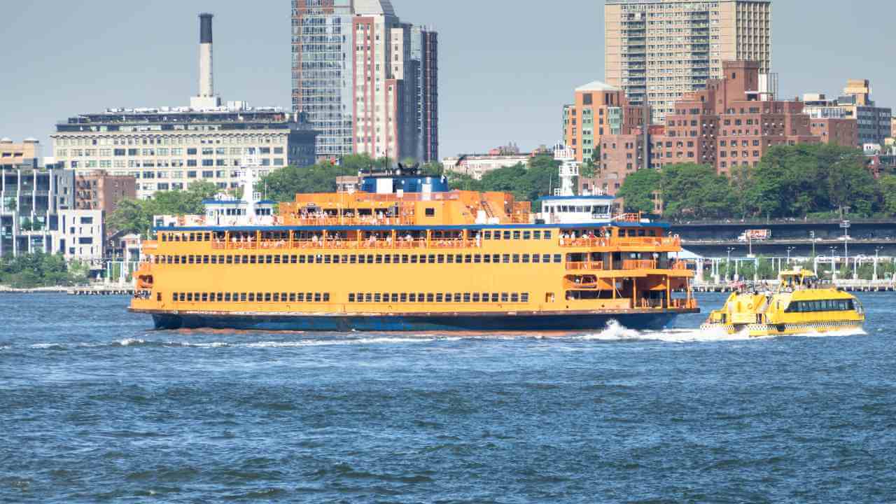 a large orange ferry traveling on the water next to a large city