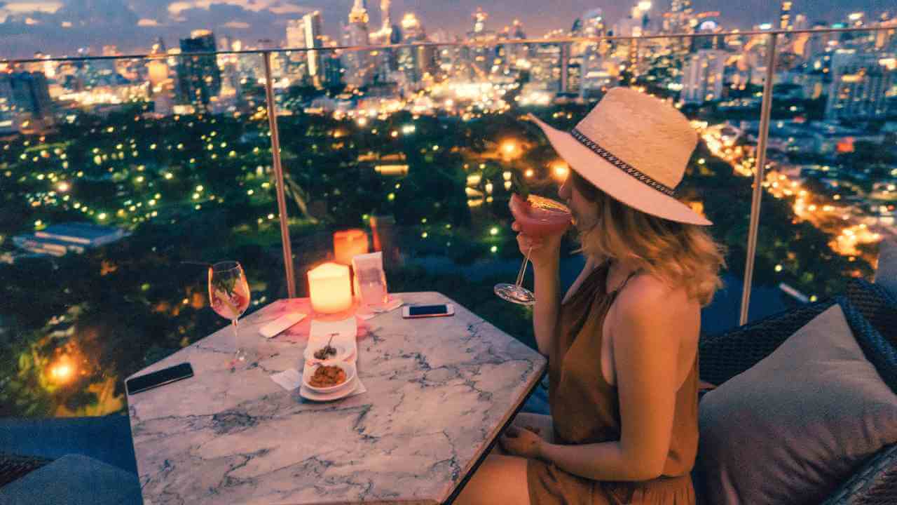 a person in a hat sitting at a table with a view of the city at night