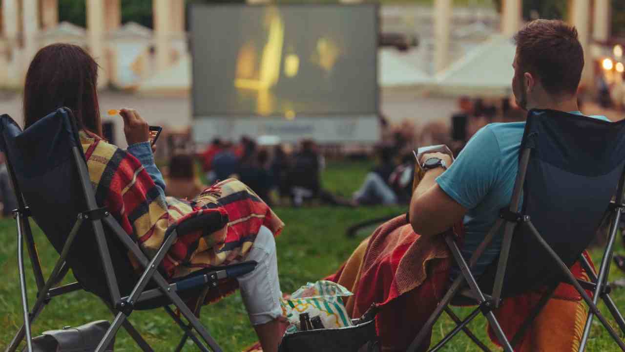 two people sitting in lawn chairs watching an outdoor movie