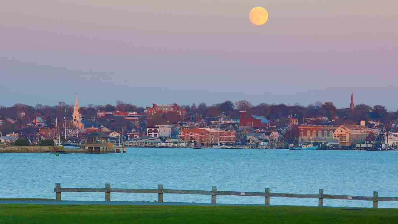 a full moon rises over the water in front of a town