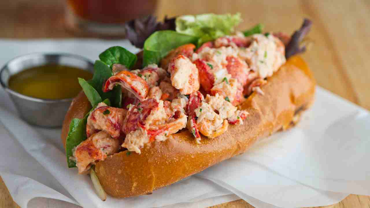 a lobster roll on a bun with a side of dipping sauce