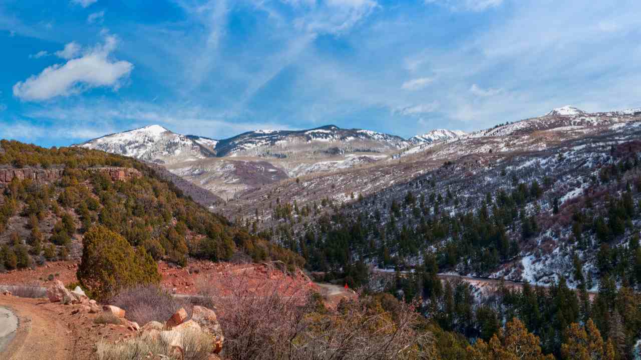 a scenic road in the mountains with snow capped mountains in the background