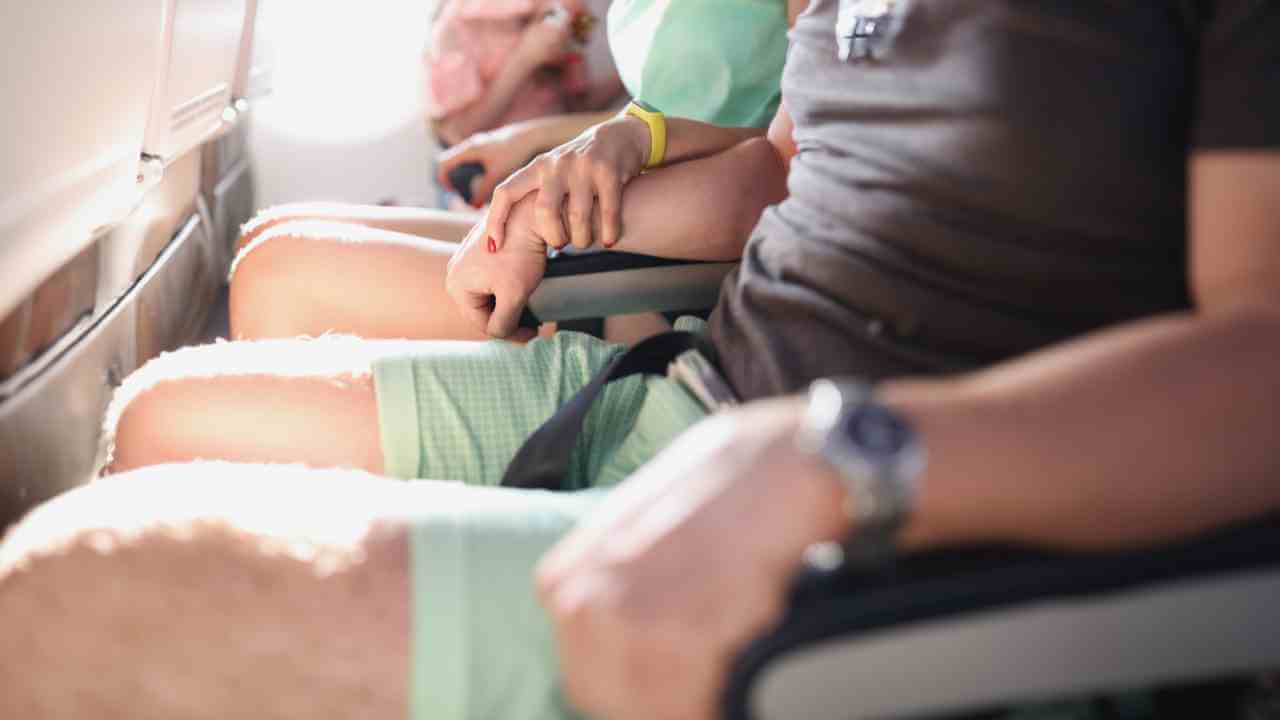 Two people sitting on an airplane with their hands on the armrests