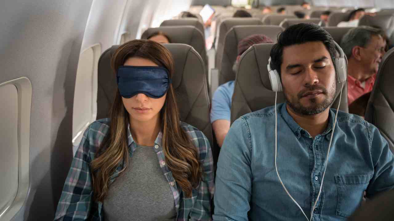 Two people sitting on an airplane with their eyes closed