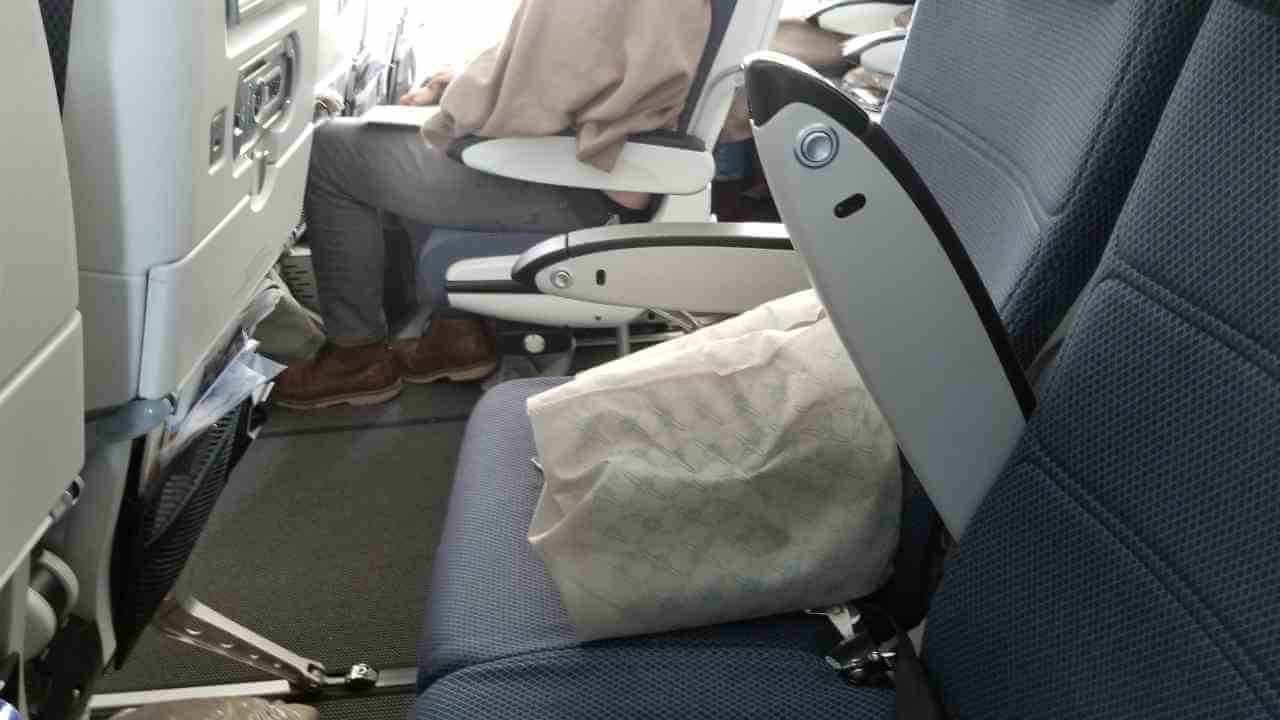 a person sitting in the seat of an airplane with a bag on the floor