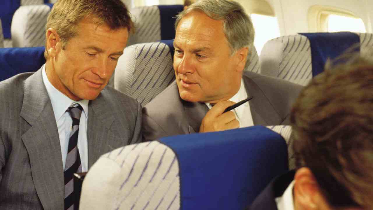 two people in business suits sitting on an airplane