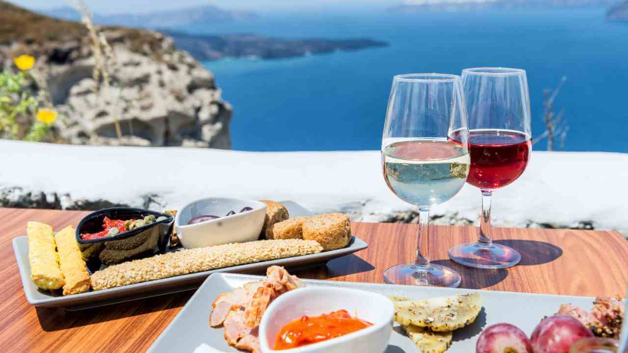 two glasses of wine and a plate of food on a table with a view of the ocean