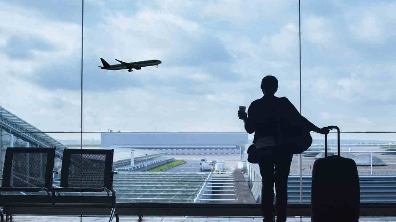 a person standing in front of a window with luggage and an airplane in the background