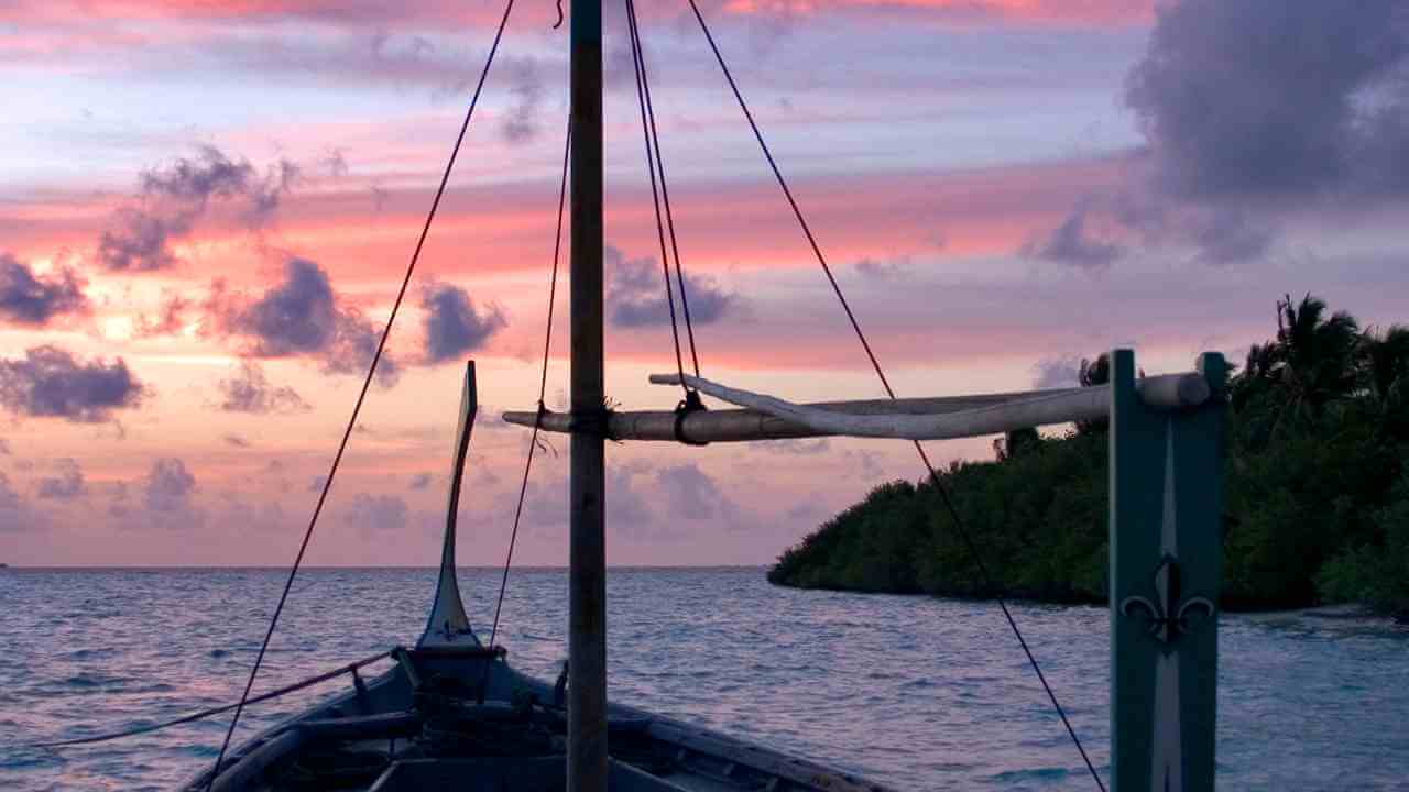 a boat in the ocean at sunset with clouds in the sky