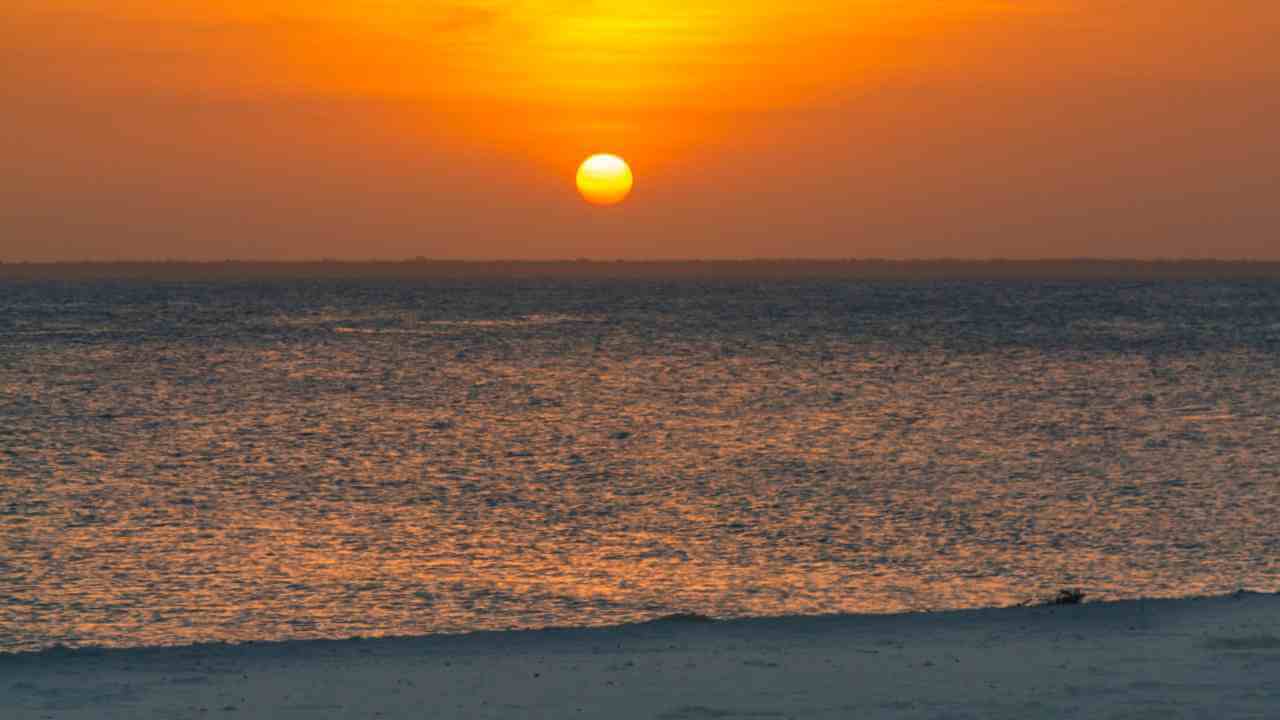 the sun is setting over the ocean in front of a beach