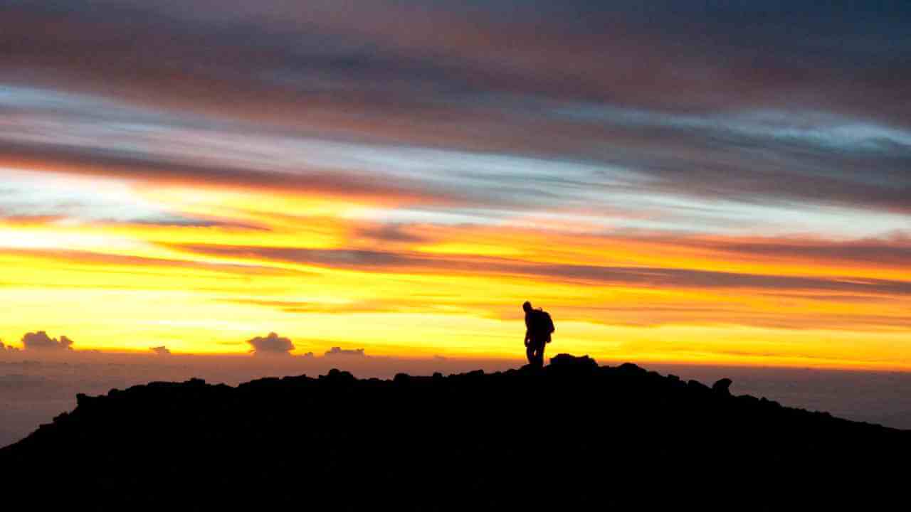 silhouette of a person standing on top of a mountain at sunset