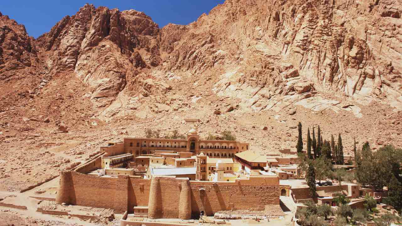 a monastery in the middle of the desert with mountains in the background