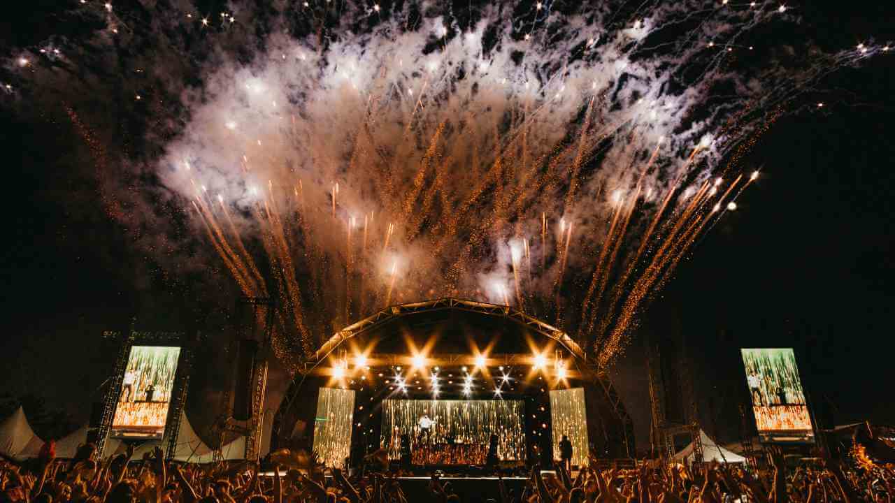 fireworks explode over a stage at a music festival