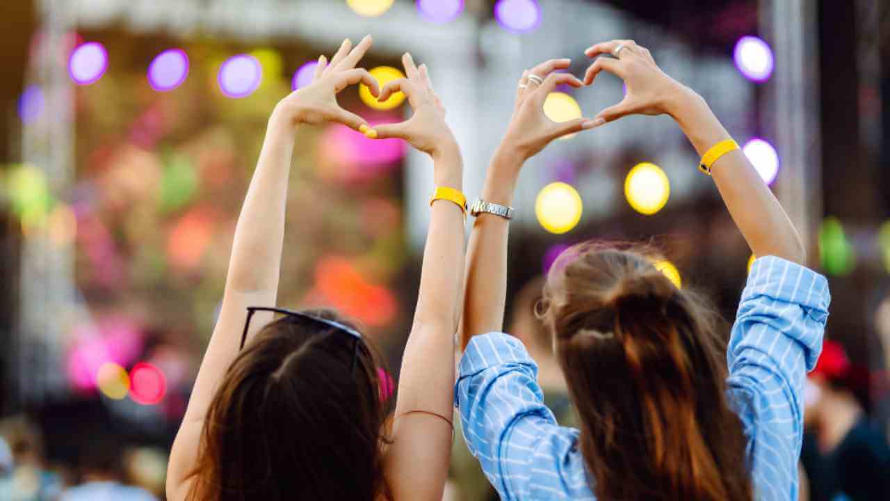 Two individuals making a heart shape with their hands at a music festival.