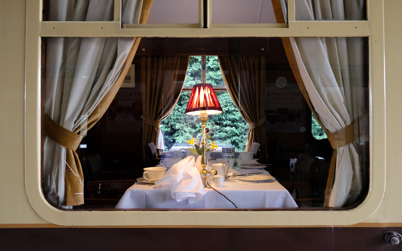 Interior view from a railway platform of a first class dining area located on a famous railway. The lit table lamp and silver service can be seen.