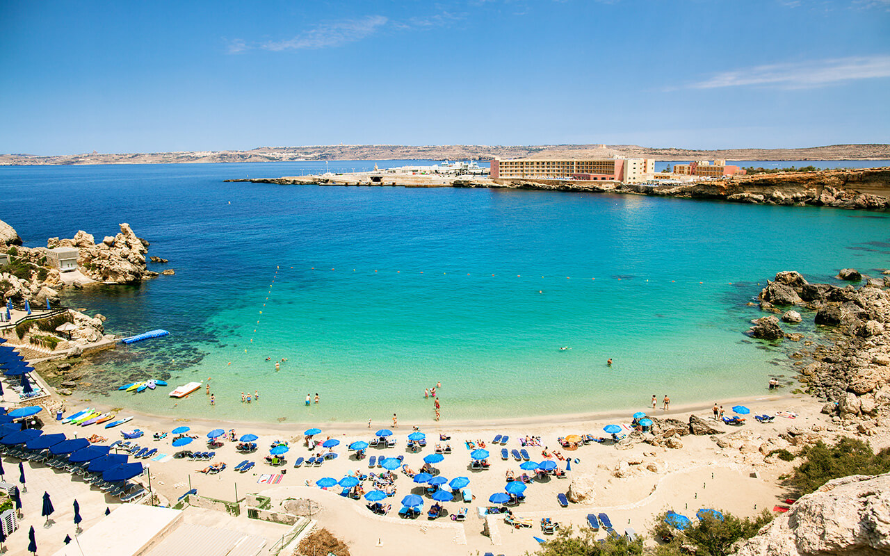 Blue umbrella on tropical beach with white sand, turquoise sea water and blue sky at deserted island in Malta, Paradise bay.