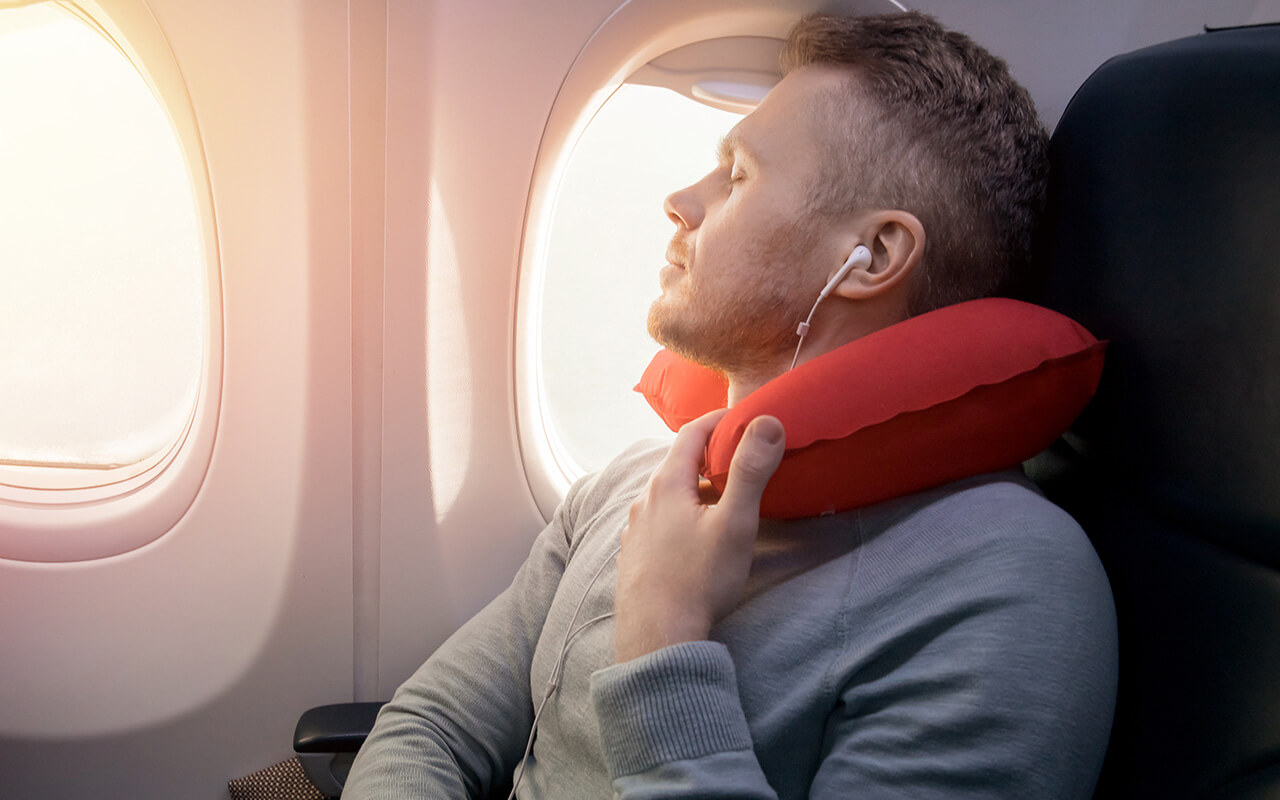 Male passenger of airplane listens to music and enjoys pillow for sleeping in chair.