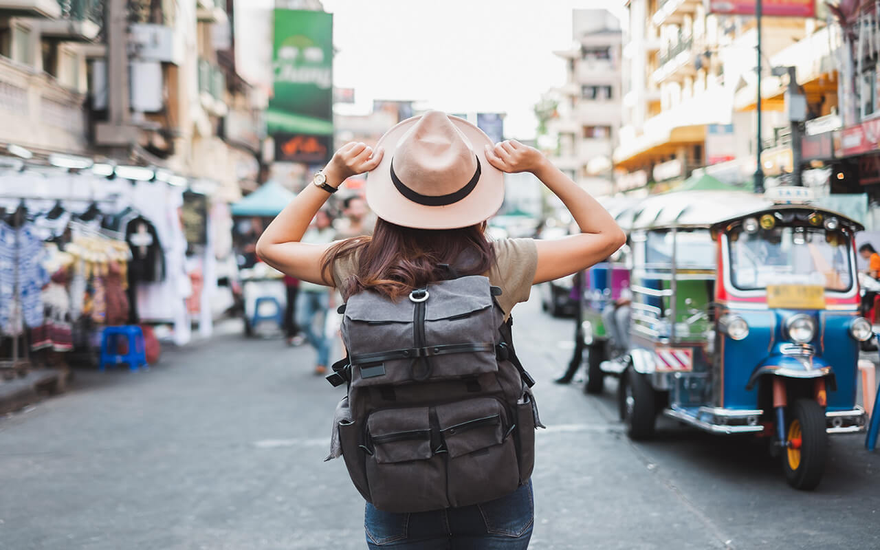 Female tourist wearing a hat and backpack looking up at skyscrapers