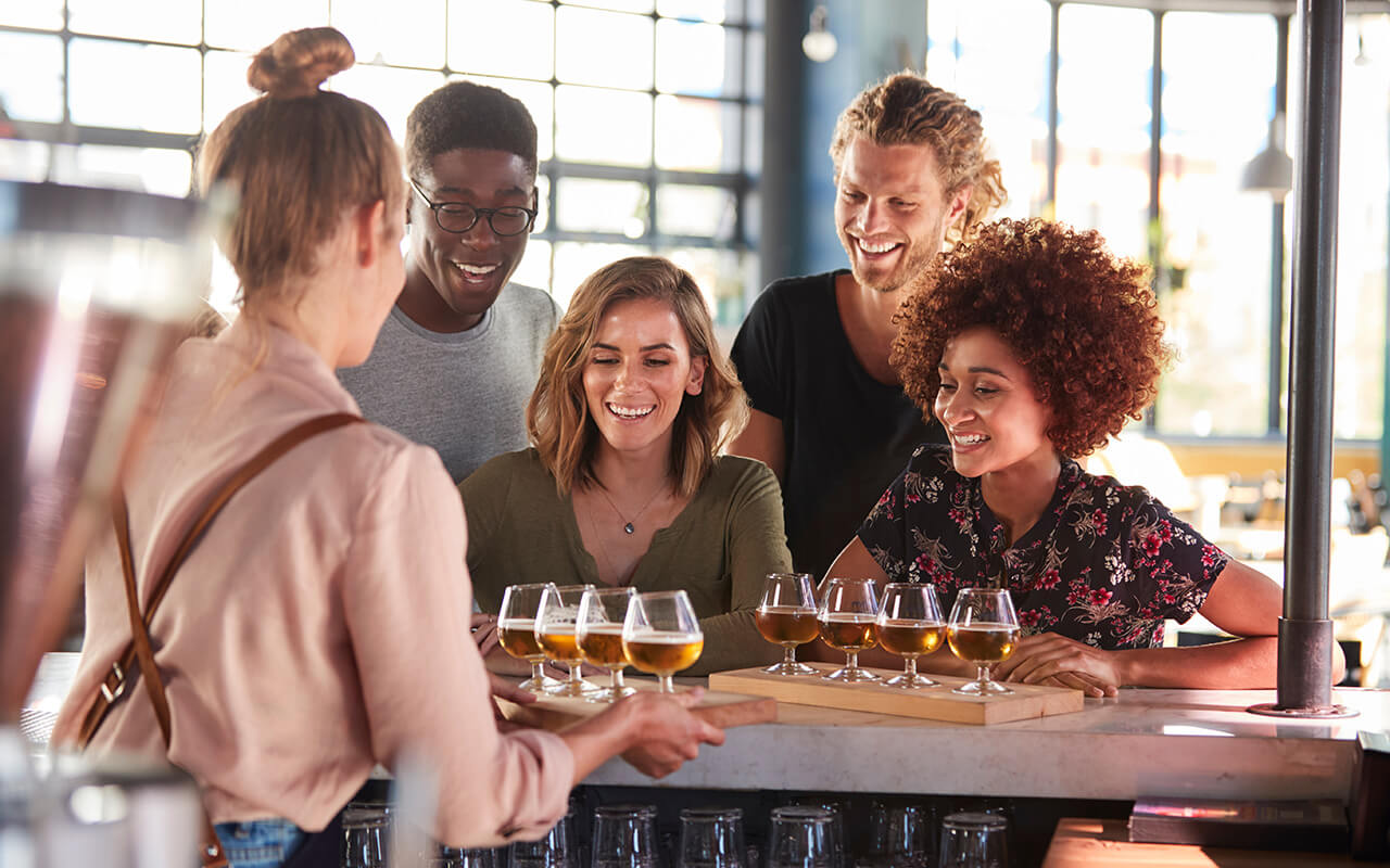 Waitress Serving Group Of Friends Beer Tasting In Bar