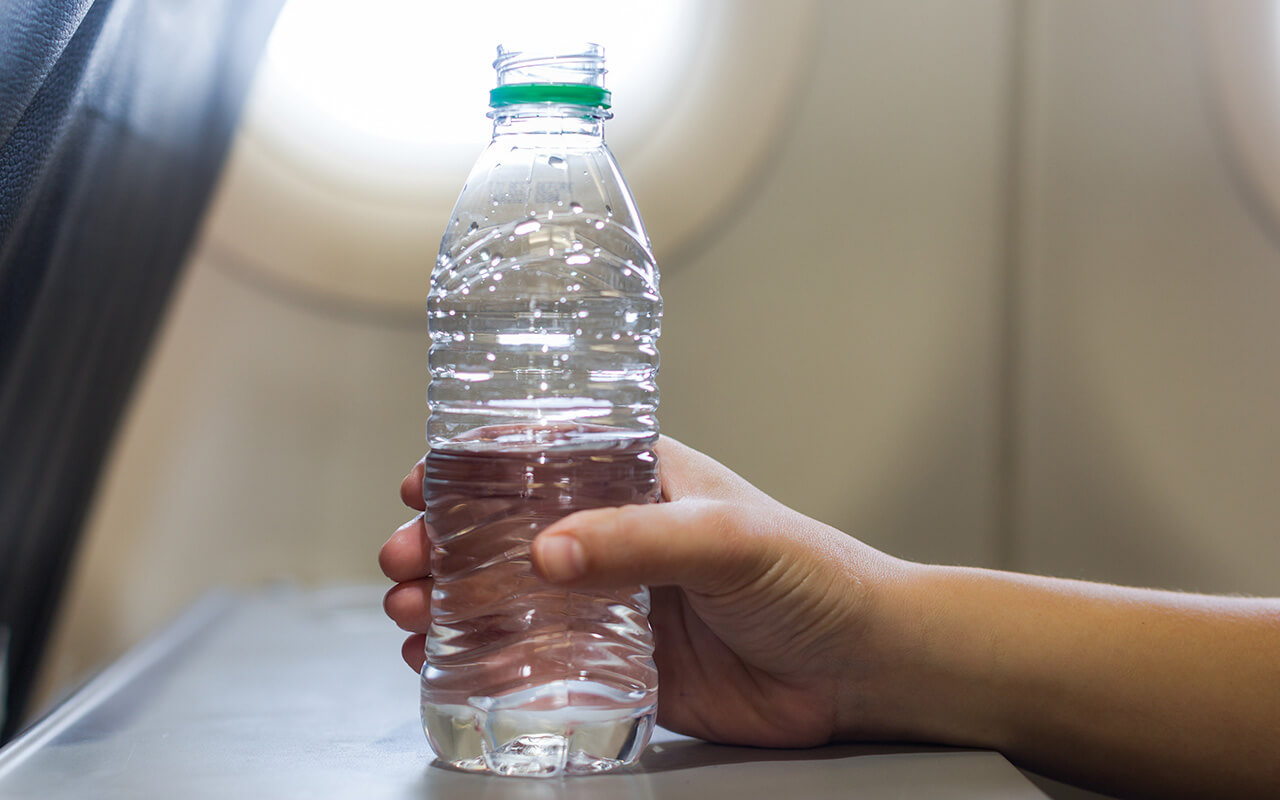 A passenger woman on a airplane flight drinking a bottle of water.